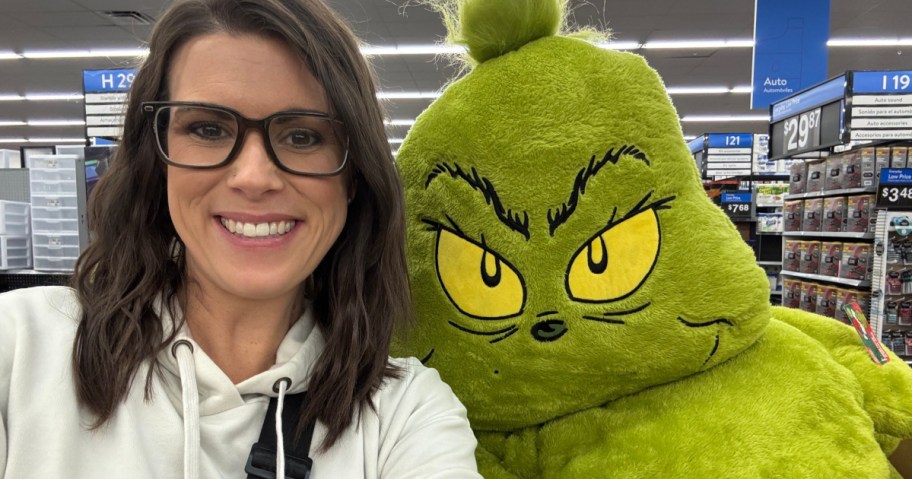 woman posing in walmart store next to jumbo grinch plush