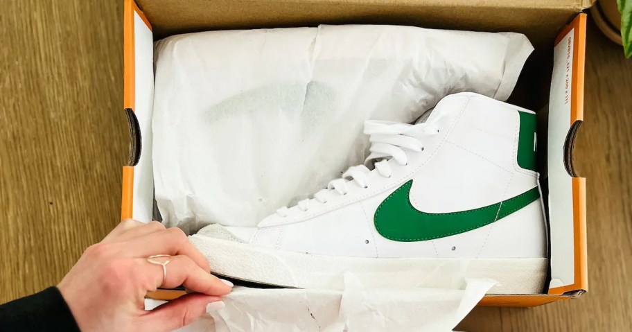 hand touching a shoe box with nike blazer shoe inside