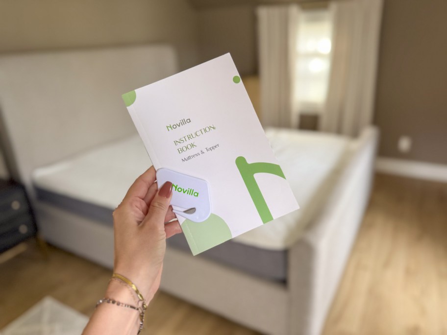 Hand holding the Novilla mattress instruction book in front of a new novilla bliss mattress