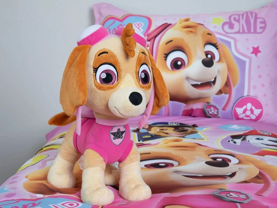 A Paw Patrol Sky Plush Dog Toy on a bed with paw aptrol sheets