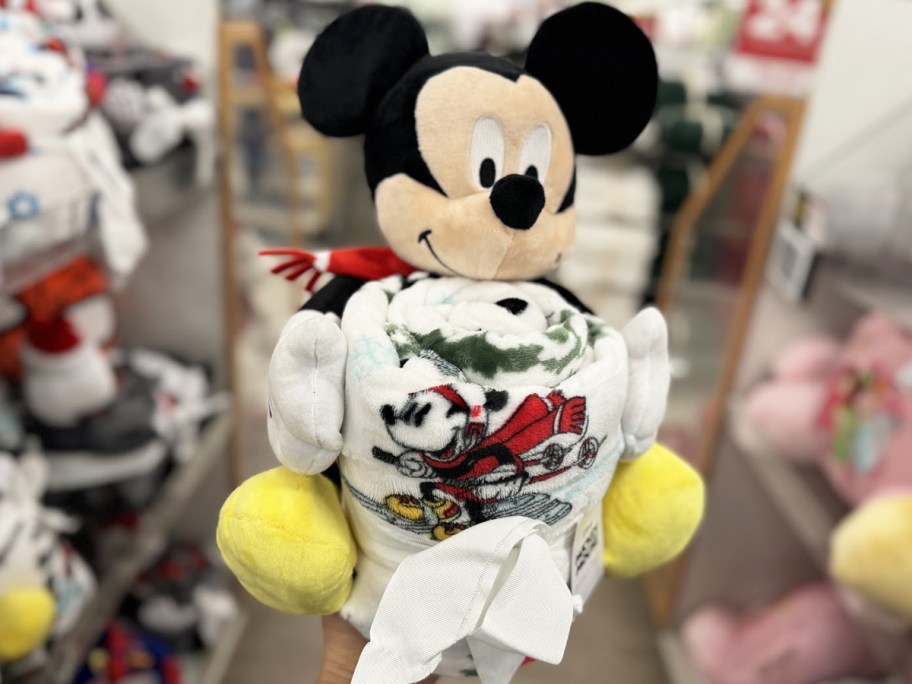 hand holding up a Mickey Mouse plush and throw blanket set in store