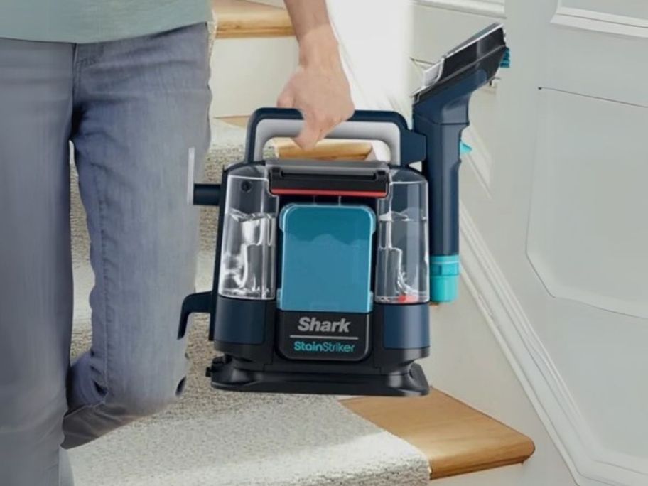 person holding Shark StainStriker Portable Carpet & Upholstery Cleaner while walking down the stairs