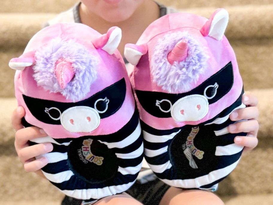 Little girl holding two Halloween Unicorn Squishmallow Slippers