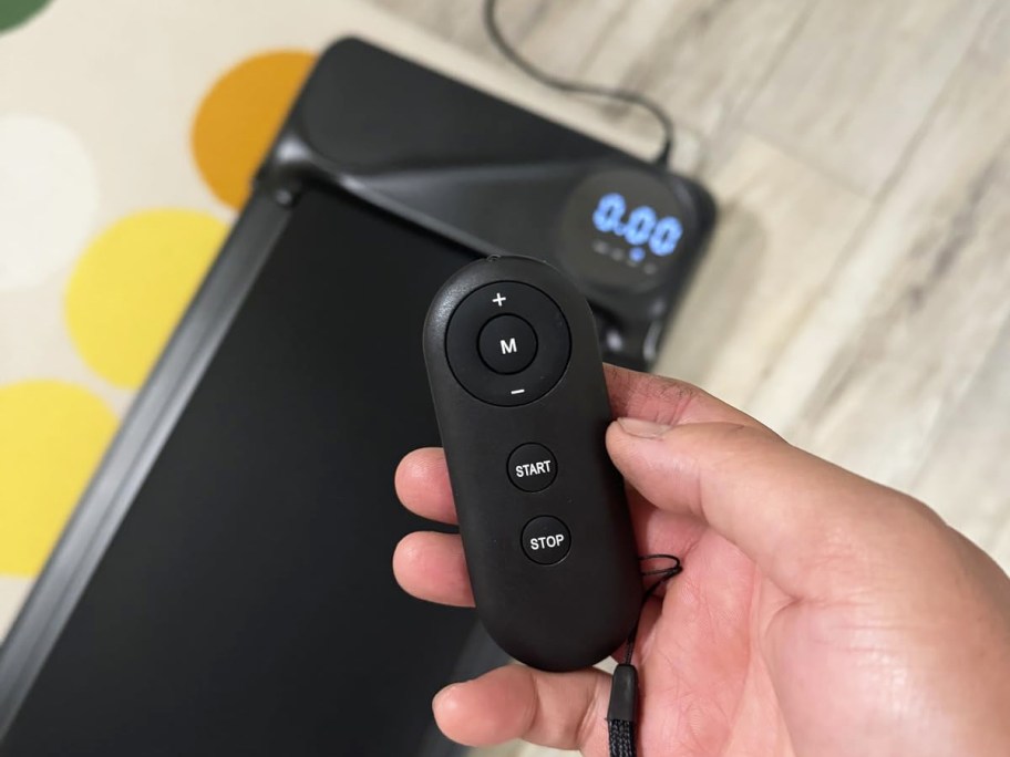 hand holding remote to walking pad in background