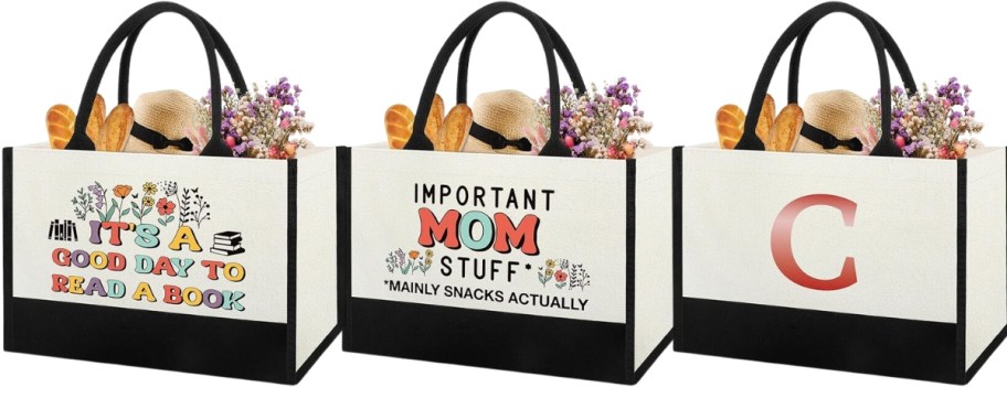 3 cream and black tote bags, one has flowers and says "it's a good day to read a book", one says "Important Mom Stuff - mainly snacks actually", and the other had a gold "C" initial on it