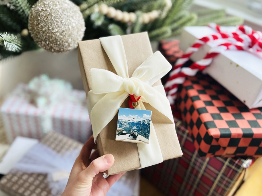 hand holding a wrapped present with a photo ornament on top