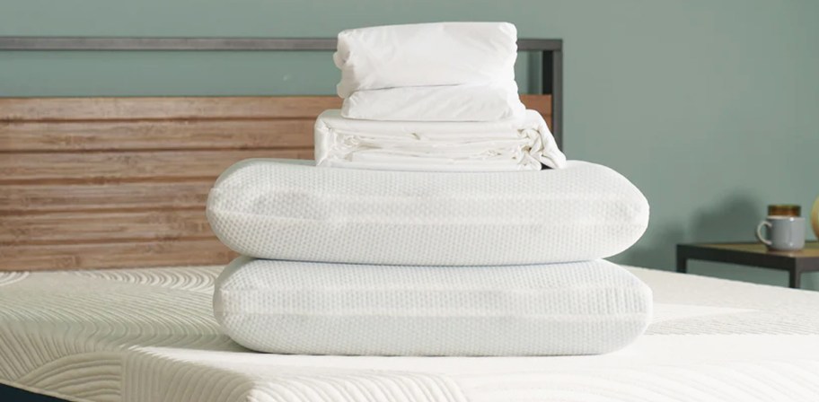 folded stack of sheets on top of pillows on bed