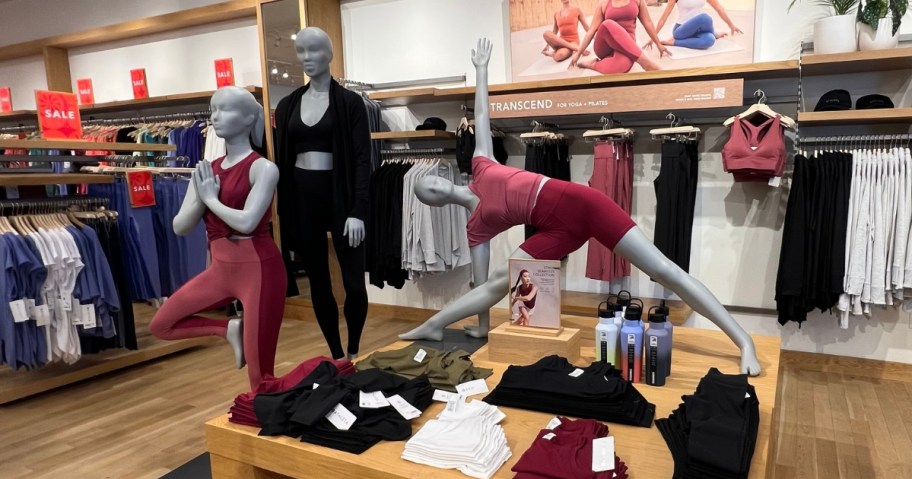 the inside of an Athleta clothing store with a display with mannequins wearing Athleta workout clothing, clothing on table beside them and racks behind them