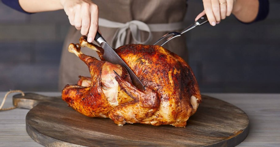 woman carving a turkey on a wooden cutting board