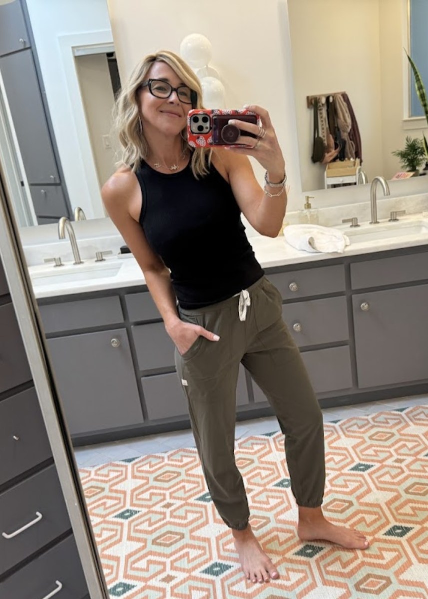 woman taking a selfie wearing a black tank top and green jogger pants
