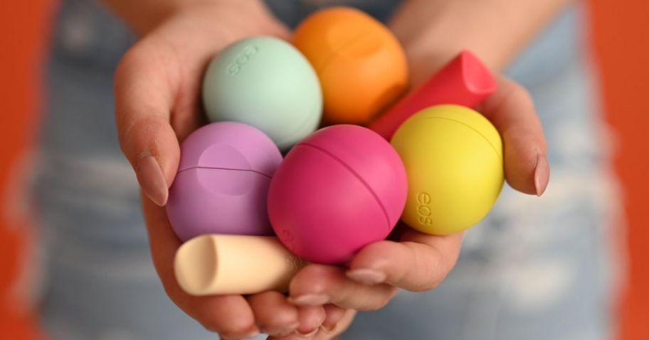 woman's hand holding a whole bunch of eos lip balms in the cupped palms