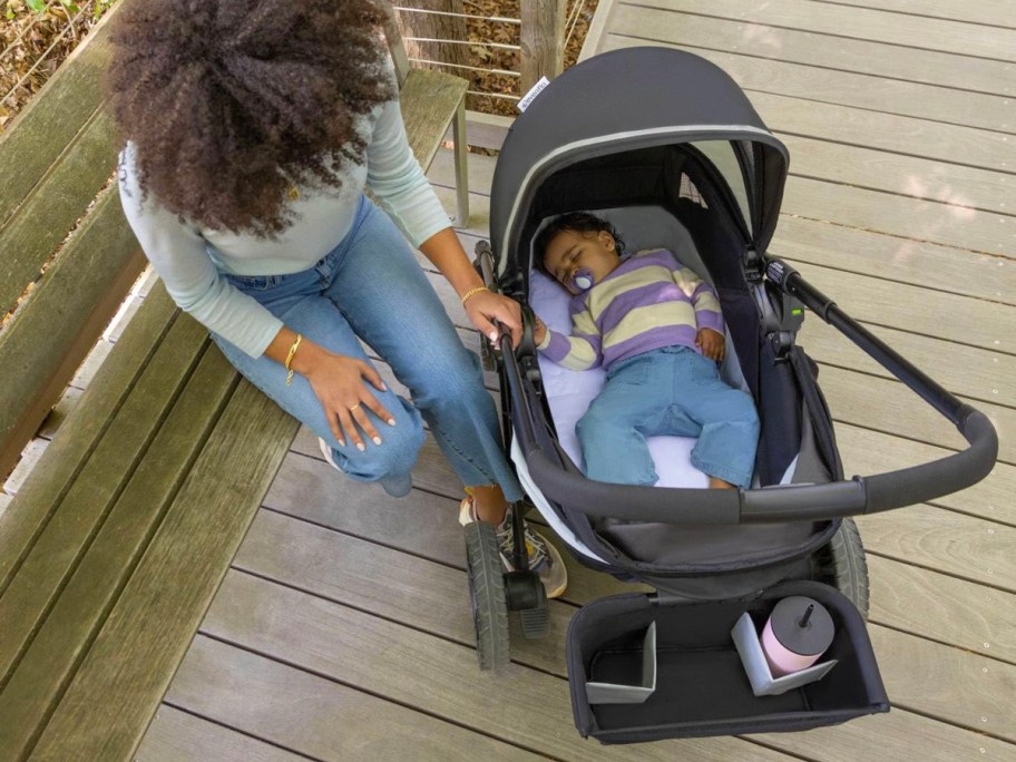 woman sitting next to stroller wagon with baby sleeping in bassinet 