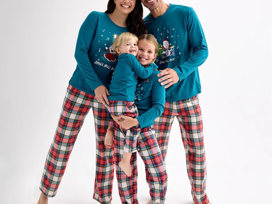 mom, dad, little girl, and toddler boy wearing matching Christmas pajamas that have red plaid pants and teal green tops with a snowman on them