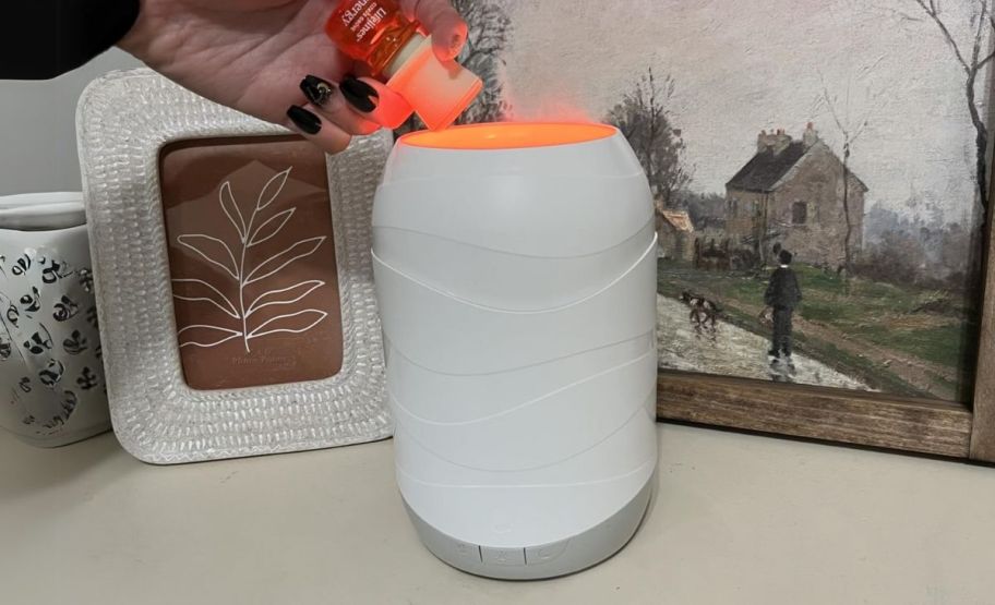 a womans hand adding essential oil to a lifelines aroma therapy wave diffuser 