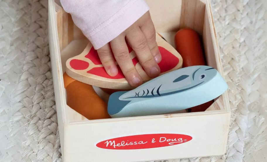 a kids hand reaching into a wooden box of wooden play food