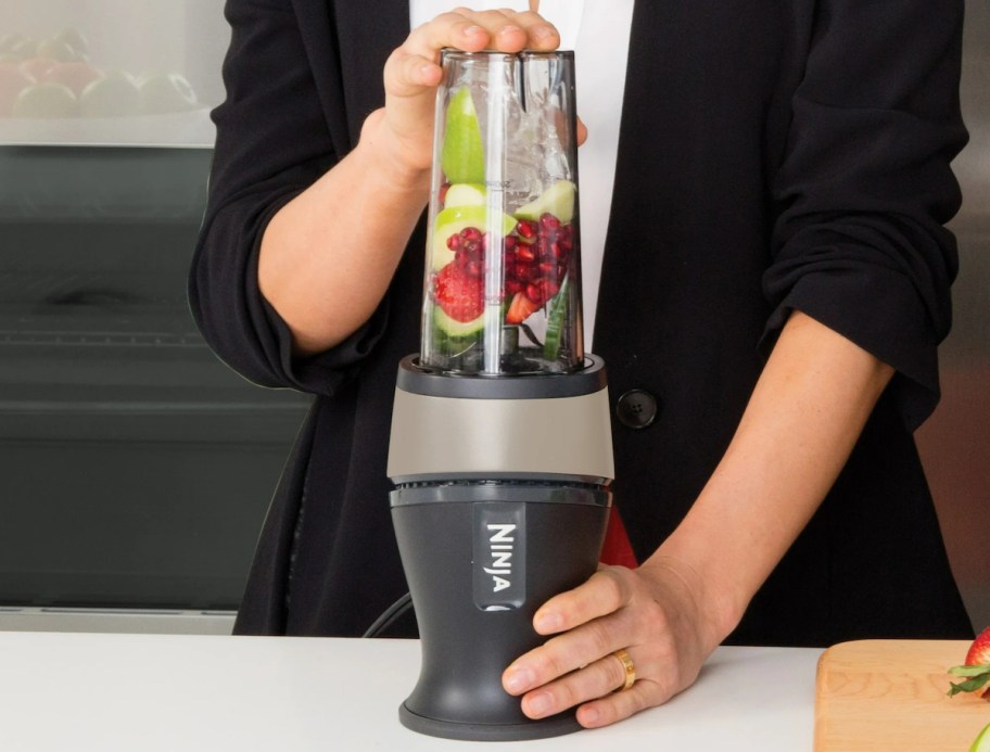 woman holding ninja blender on countertop with food