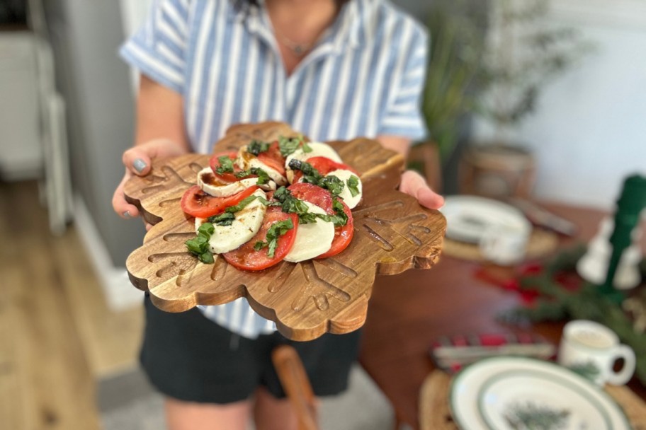 woman holding a snowflake charcuterie board with a caprese salad shaped like a wreath on it