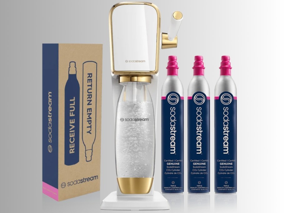 a white and gold SodaStream Art machine with a bottle with carbonated drink, a box with CO2 Cylinders and 3 cylinders on each side