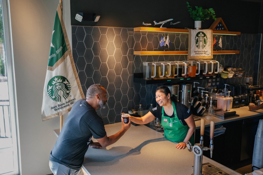 woman at starbucks handing a man in a navy blue shirt a coffee cup across a counter