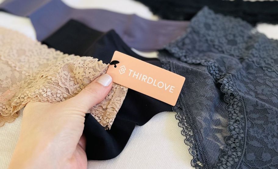 a woman holding a brand tag attached to a pair of beige lace underwear