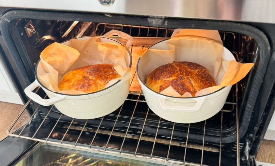 two white dutch ovens inside of oven with sourdough loaves of bread