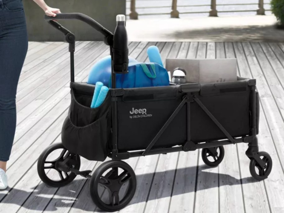 a woman pushing a stroller wagon that is full of items