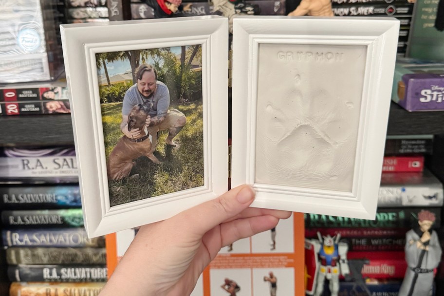 hand holding a pup paw print picture frame with photo of man and dog