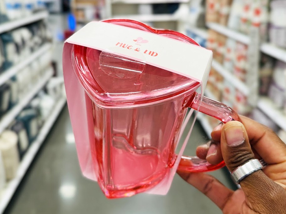 hand holding up a pink heart shaped mug