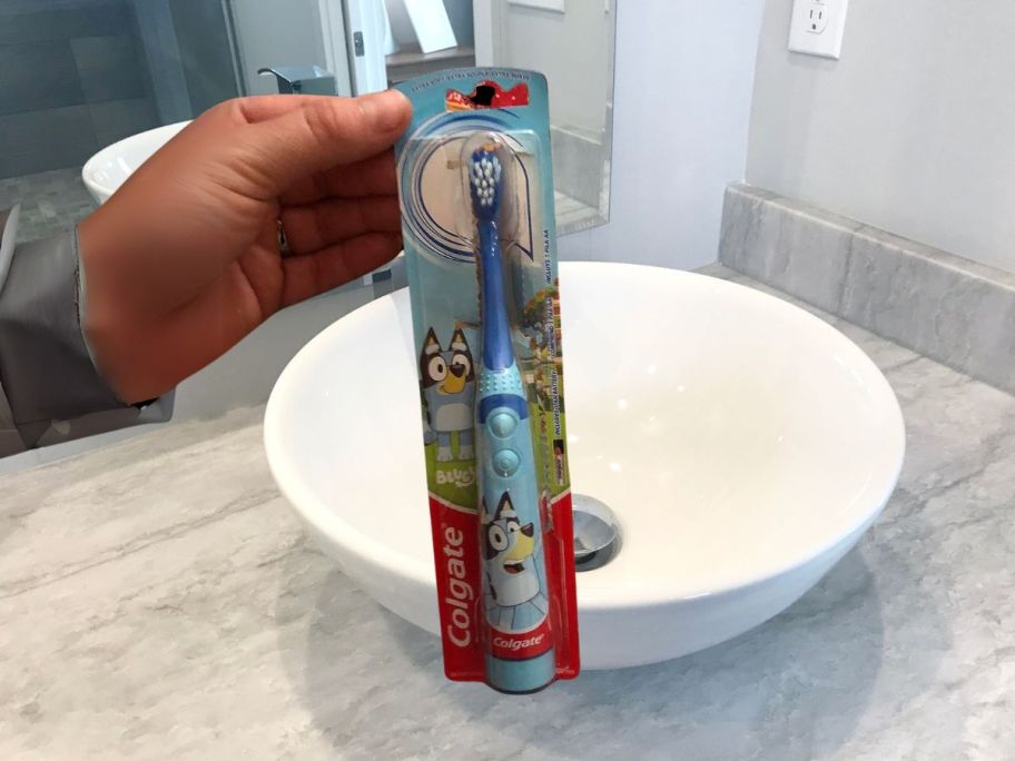 hand holding Colgate Kids Battery Powered Bluey Toothbrush in bathroom