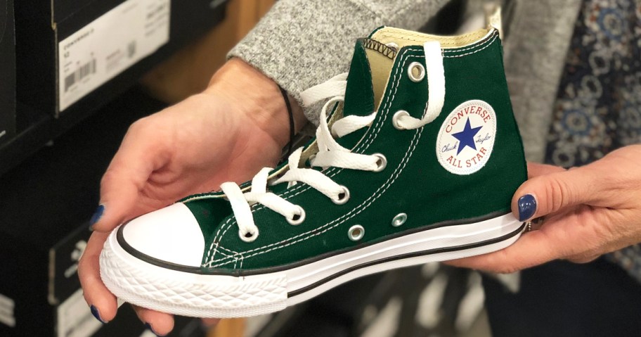 woman holding up a dark green converse high top sneaker in store