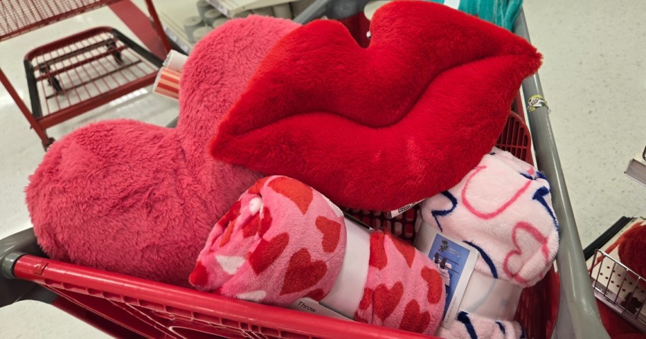 a Target shopping cart with a pink heart pillow, red lips pillow, pink and red hearts throw blanket, and pink and blue hearts throw blanket in it