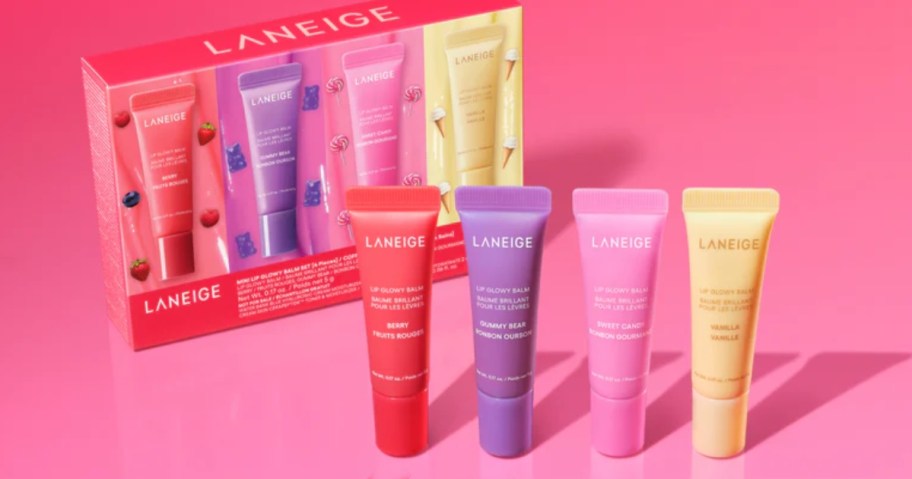 a 4 piece set of Laneige glowy lip balms in dark pink, purple, yellow, and light pink colors next to the box it onlinees in, on a pink background