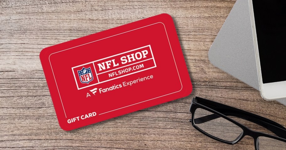 a red Fanatics NFLShop.online Gift Card on a desk - part of a pair of black framed glasses and a white smartphone are off to the side 