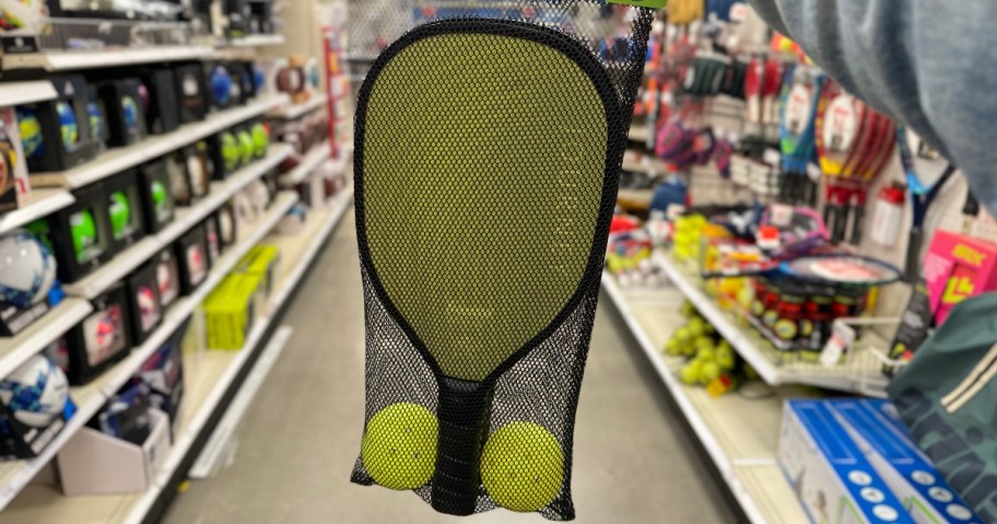 hand holding a set of 2 Pickle paddles and 2 yellow balls in a black mesh bag that it's packaged in