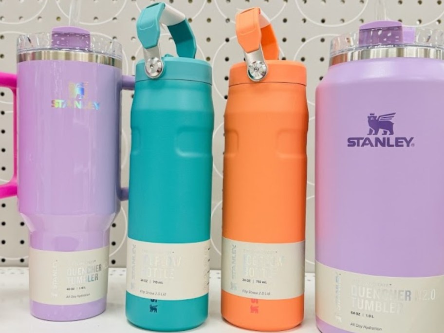 a lavender Stanley tumbler, a teal and an orange Stanley water bottle, and a lavender Stanley large tumbler on a Target store shelf