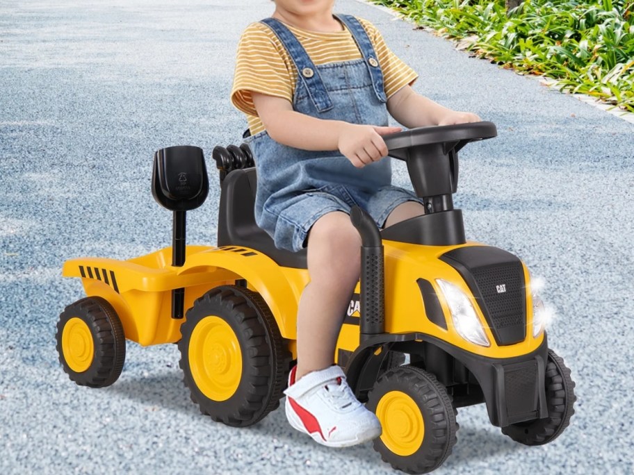 little kid riding on a yellow toy CAT tractor that has a pull trailer