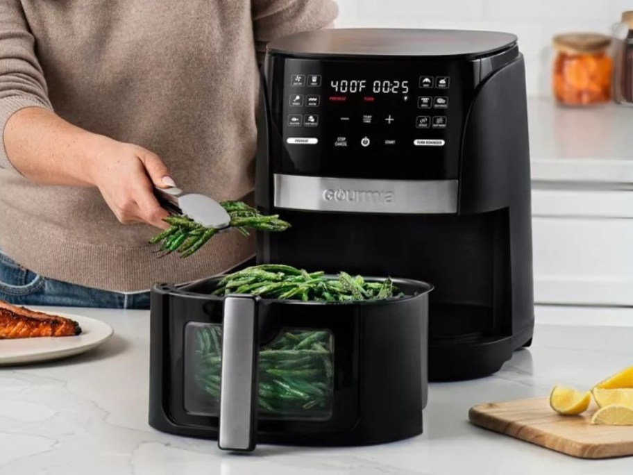 a woman getting food out of a black air fryer on a kitchen table