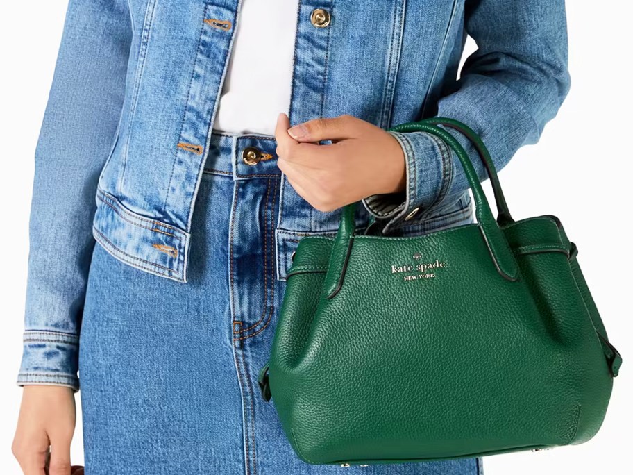 woman in a denim outfit holding a green kate spade purse