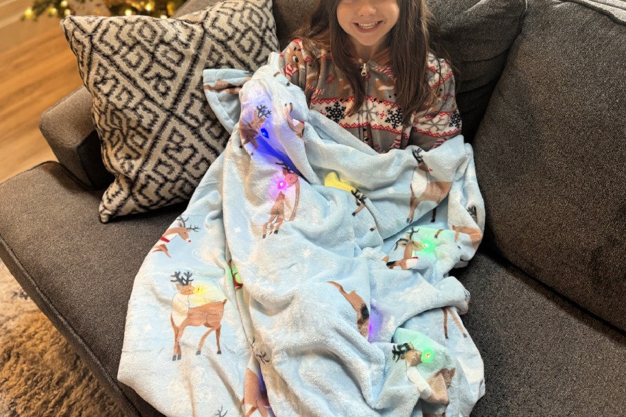 girl wrapped up in an LED Christmas Blanket that features illustrated reindeer with light-up noses