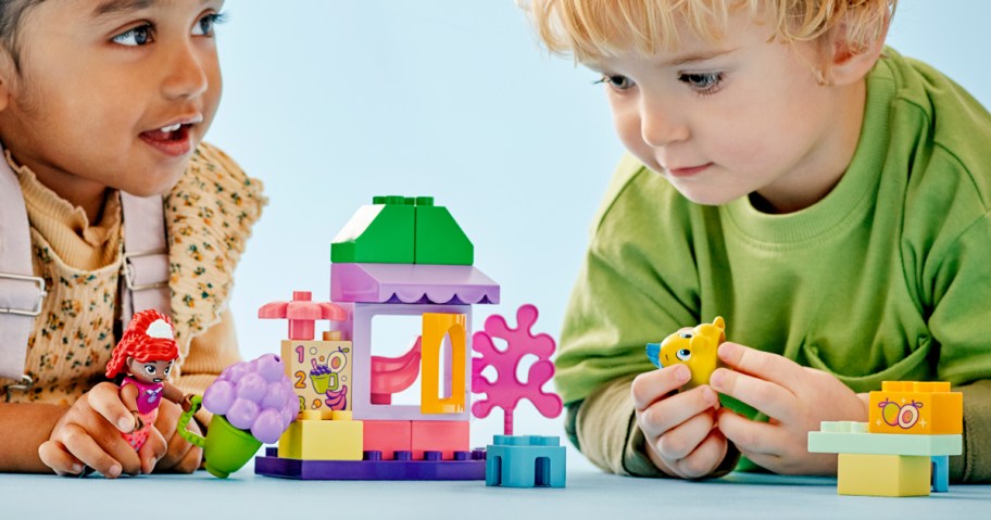 two kids laying on floor playing with lego set