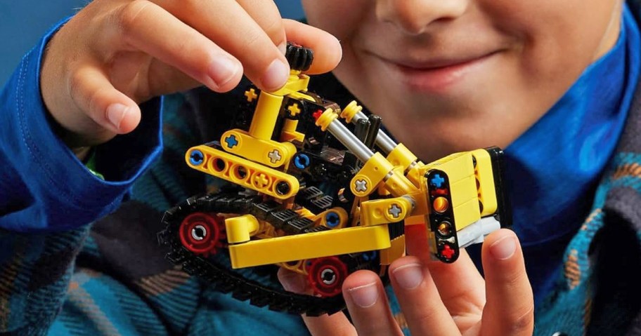 boy holding yellow LEGO Technic Heavy-Duty Bulldozer