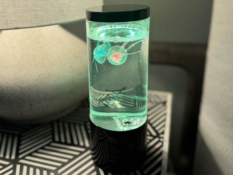 A green Merkury Innovations Jellyfish Lamp on a bed side table