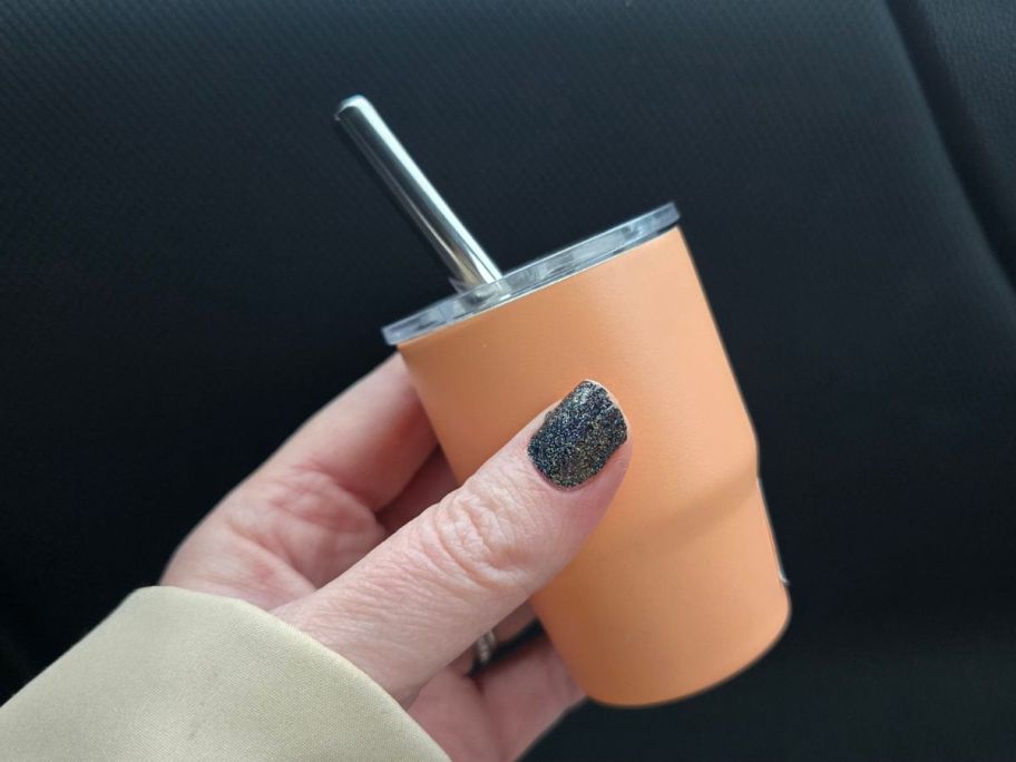 A person holding a tiny orange tumbler