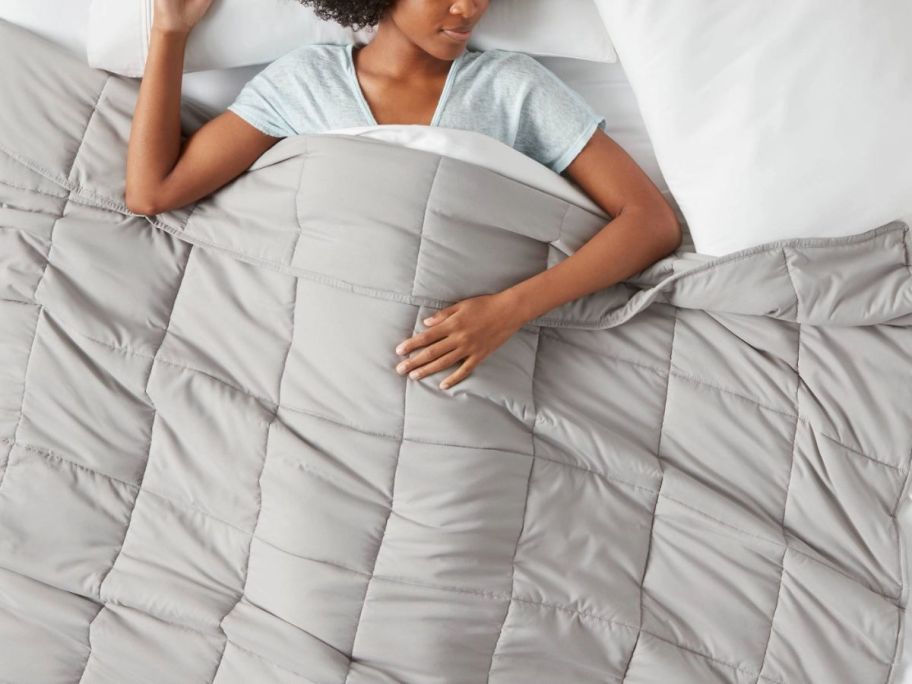 a woman sleeping under a gray weighted throw blanket draped across a bed