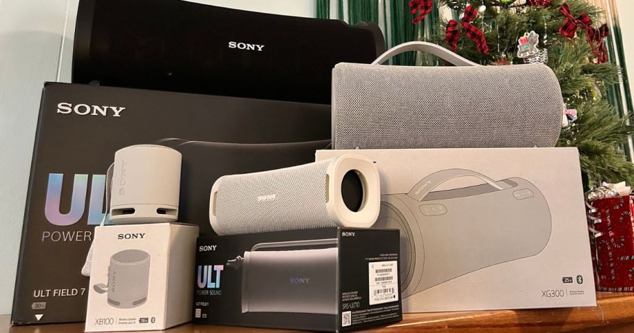 Several Sony Speakers on a desk next to a small christmas tree and wrapped gift boxes