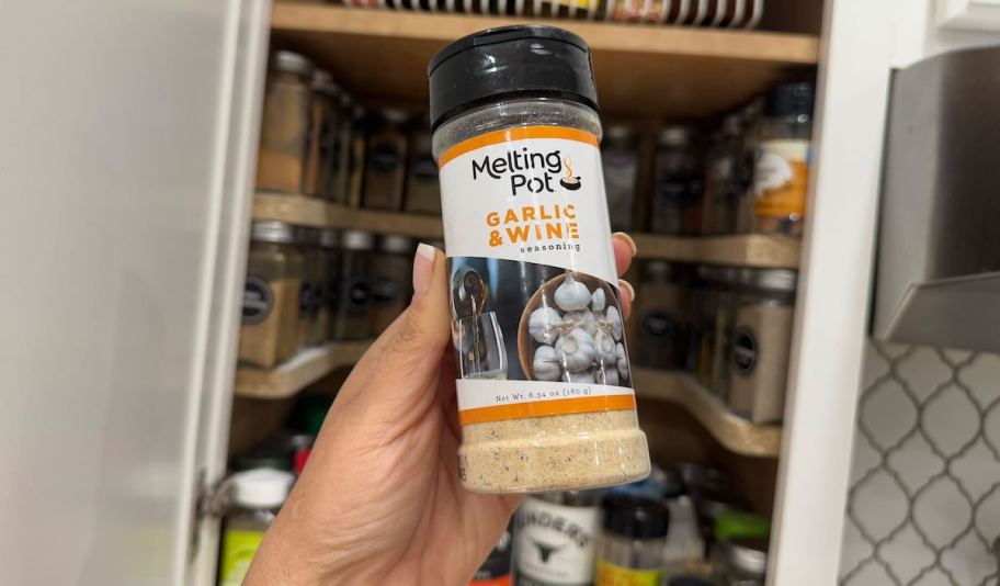 hand holding the melting pot seasoning in front of open cabinet