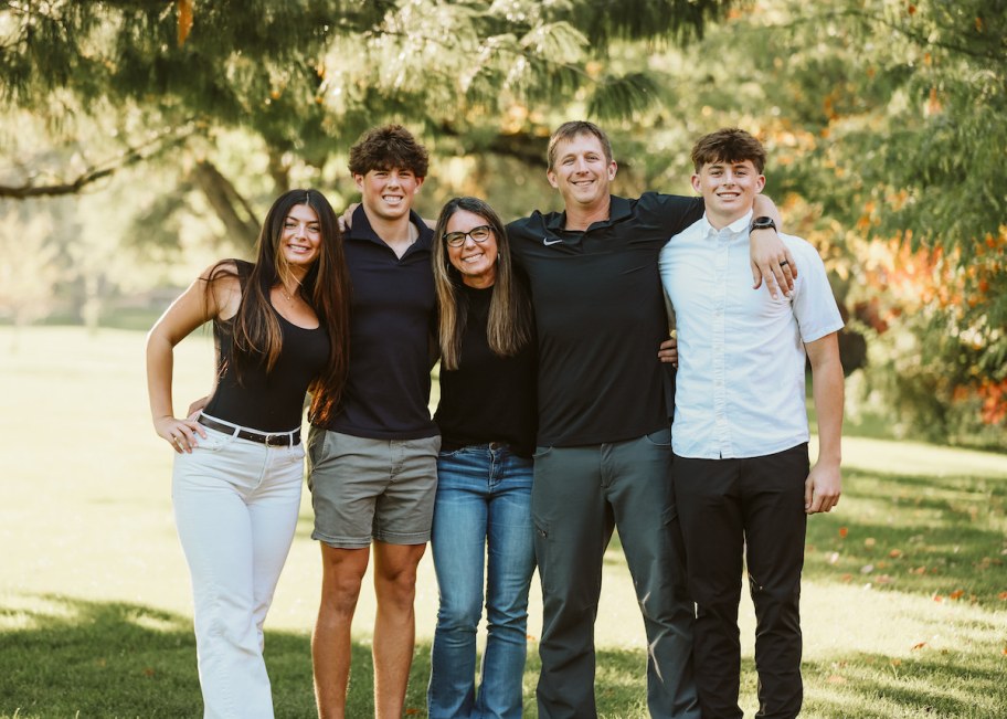 family standing together with arms wrapped around each other under large tree