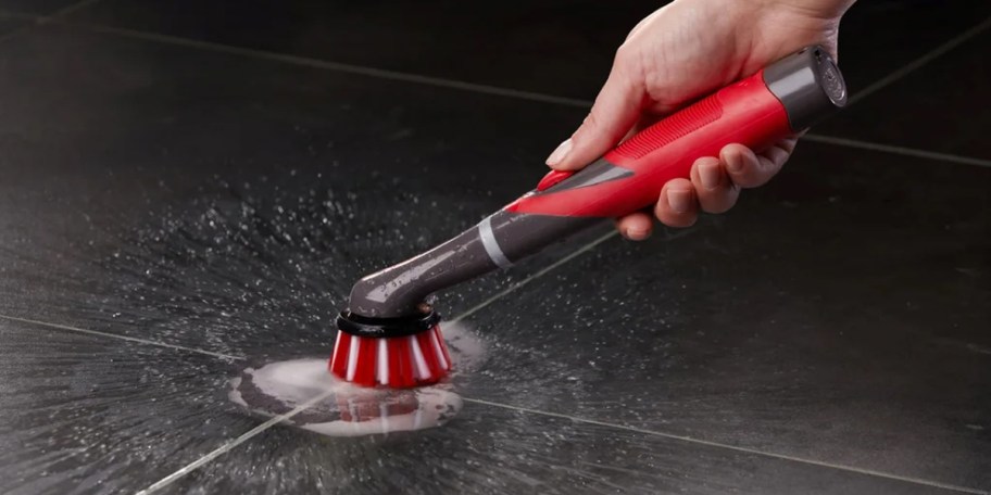 hand using red and gray rubbermaid power scrubber on tile 