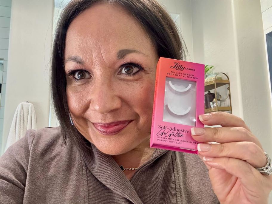 woman holding a pack of fake lashes next to face