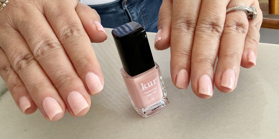 pink nail polish on table with hands sitting next to it 